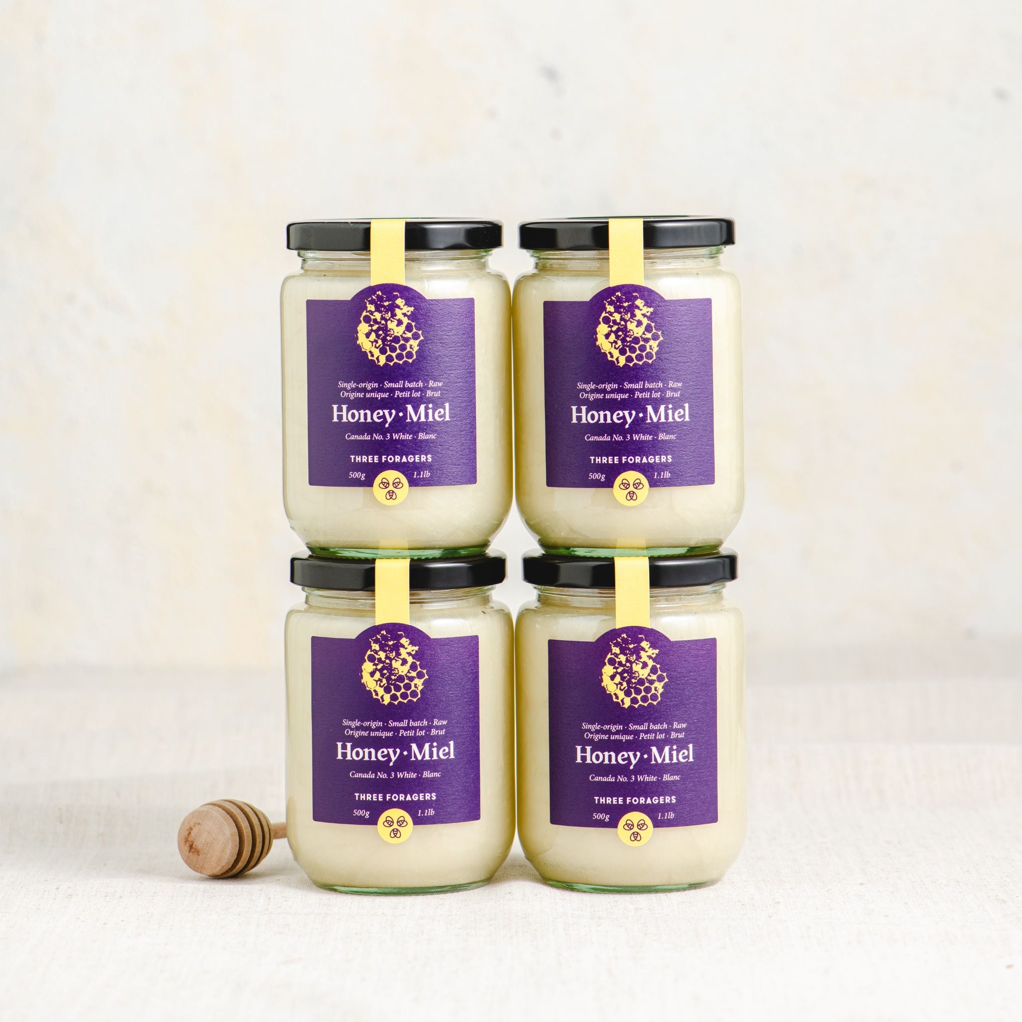 Four 500 gram jars of Three Foragers Creamed Honey next to a honey dipper