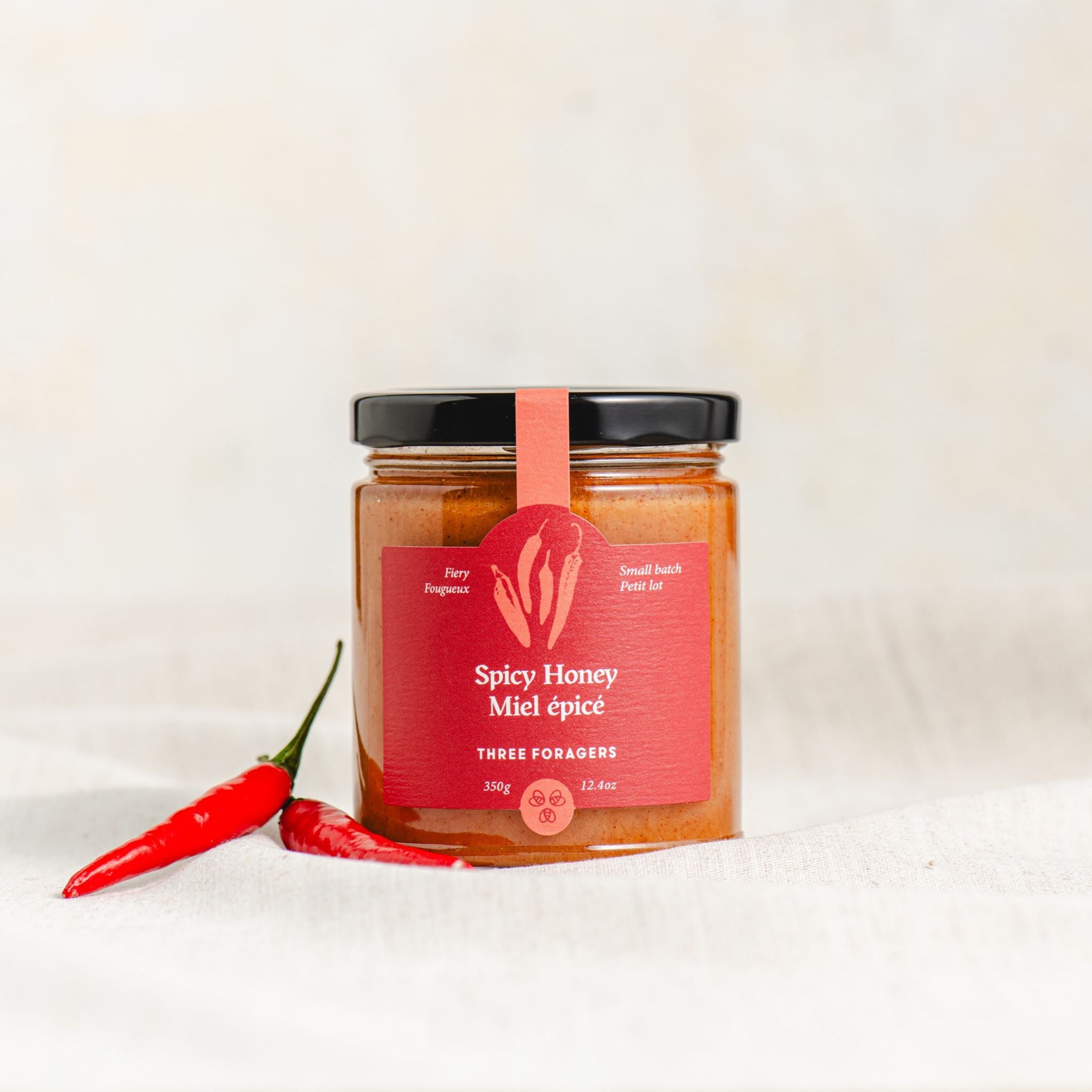 A jar of Three Foragers Spicy Honey with a couple of chilis next to it