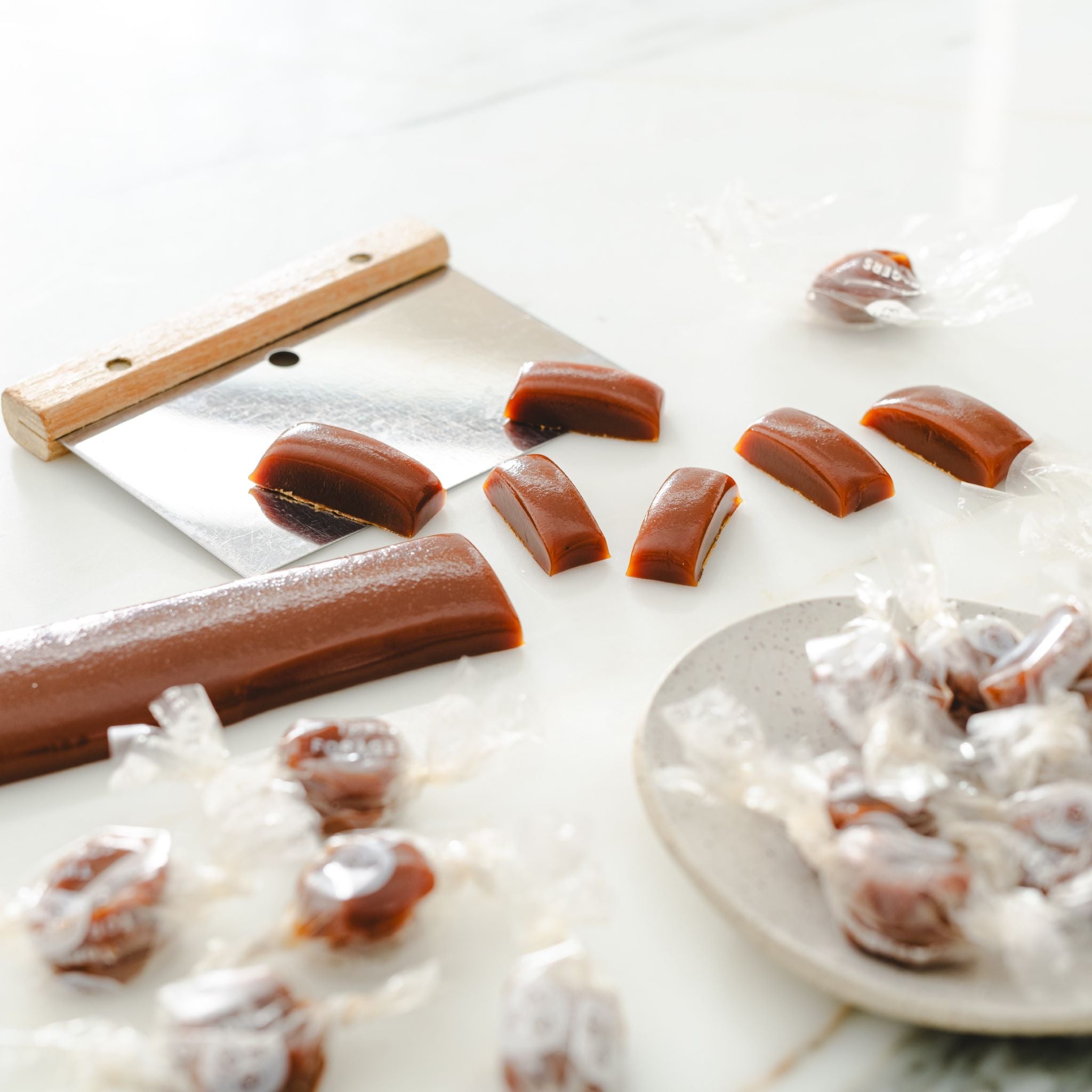 A small rectangle of uncut honey caramel with some wrapped and unwrapped honey caramels around it